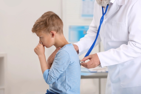 young boy coughing while getting examined by a doctor depicting signs of AC unit mold