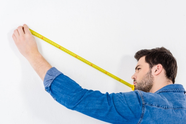 man using tape measure on the wall depicting air conditioner sizing