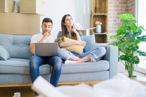 couple thinking while looking at laptop on the couch depicting deciding between will-call or automatic oil delivery