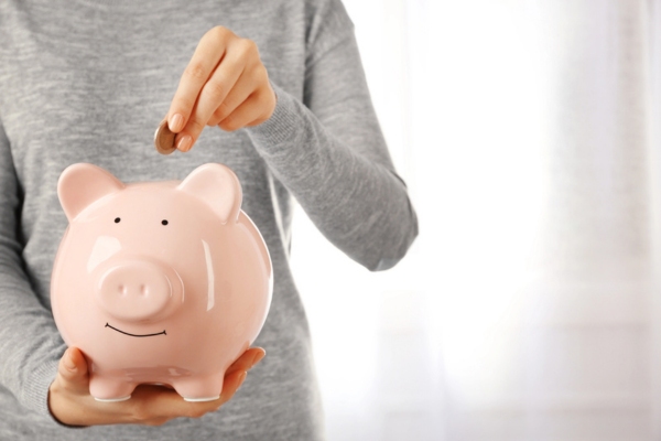 cropped view of a woman putting a coin in a piggy bank depicting reducing heating expenses