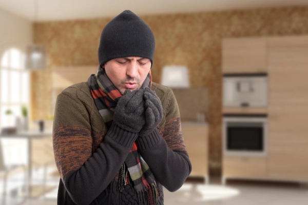 man feeling cold wearing hat, scarf, and gloves indoors depicting heating efficiency concerns